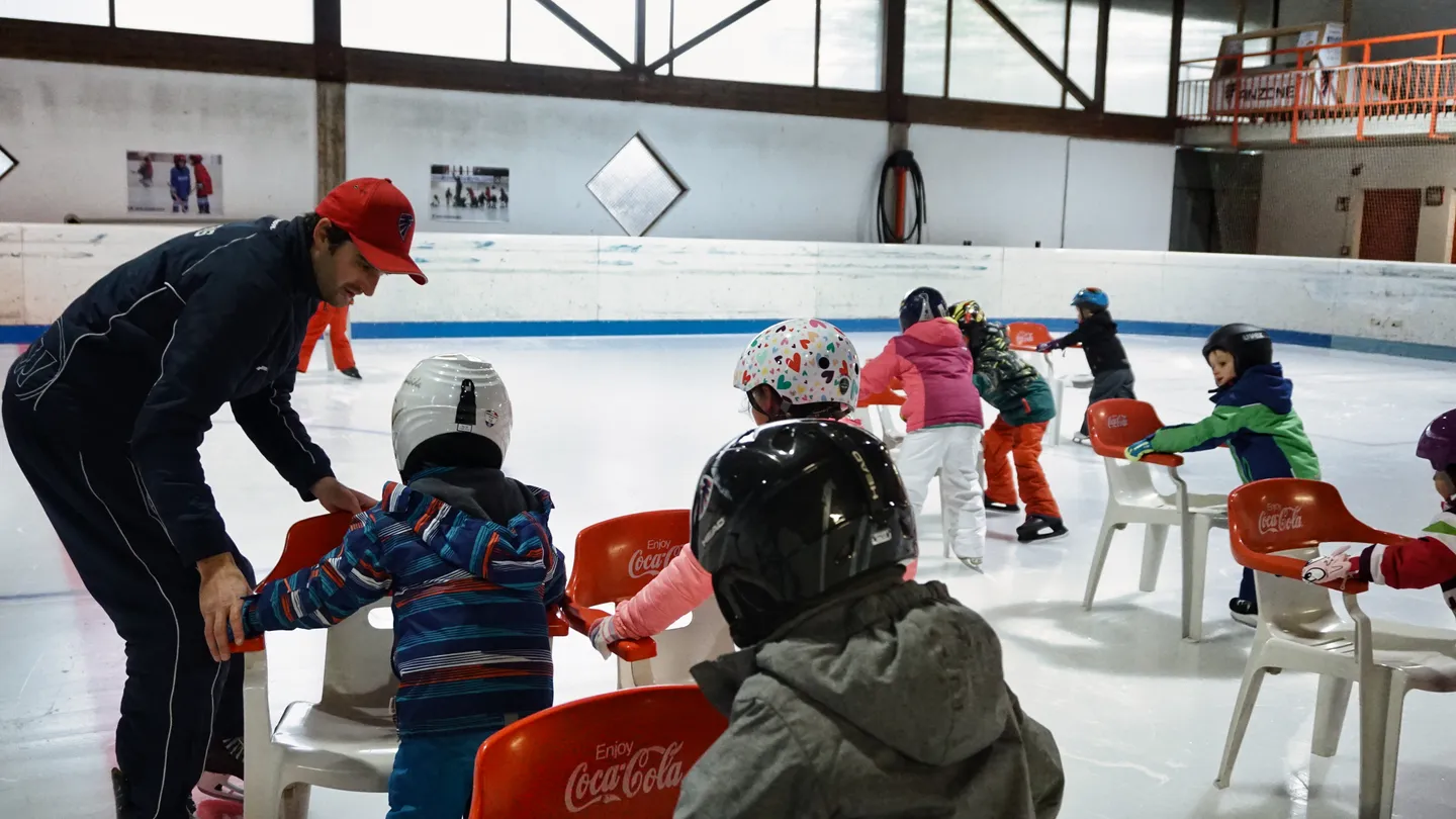 Bambini con il casco e un allenatore durante un esercizio insieme sul ghiaccio.